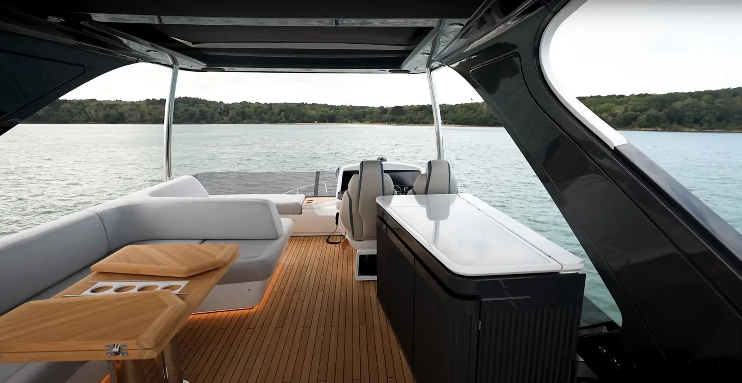 Interior of a luxury boat featuring sleek seating, wooden tables, and a stylish kitchenette, with water views and green hills.